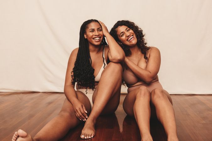 Best friends smiling while sitting in underwear in natural body photoshoot