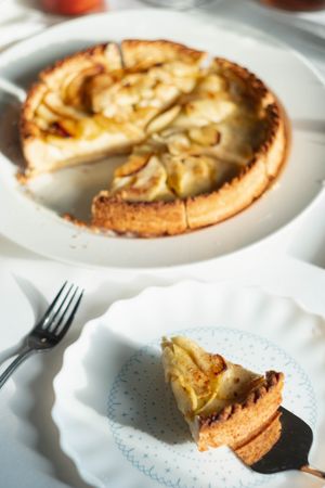 Apple tart with slice removed on ceramic plate with pie knife