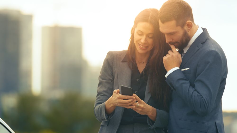 Young Couple of Business Man and Business Woman Use Smartphone and Share it.