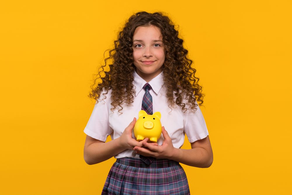 Girl in school uniform holding yellow piggy bank