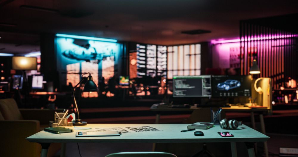 Wide Shot of Desk with Smartphone, Laptop Computer and Notebook, Placed in an Empty Creative Office at Night.