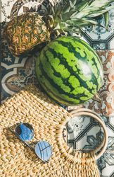 Thatched bag on pattered tiles with sunglasses, watermelon vertical composition