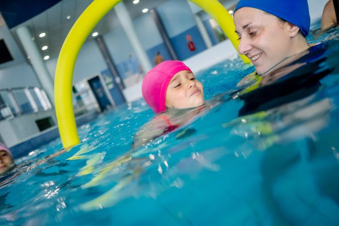 Cheerful girl swimming in pool with mother