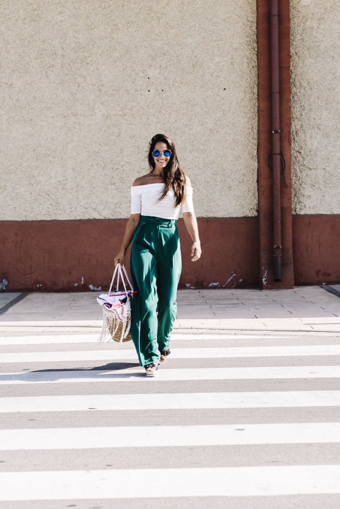 Stylish smiling woman with sunglasses holding a handbag while crossing the street