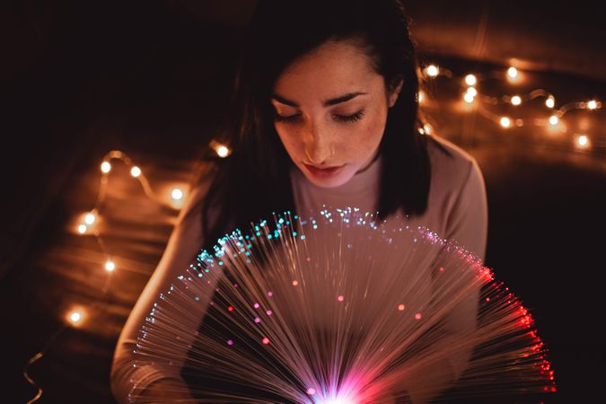 Young woman with fairy lights in darkness