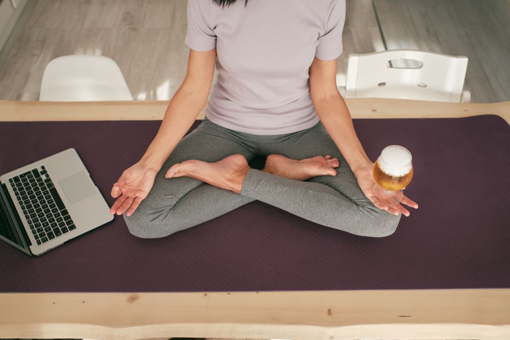 Unrecognizable female meditating with beer near laptop