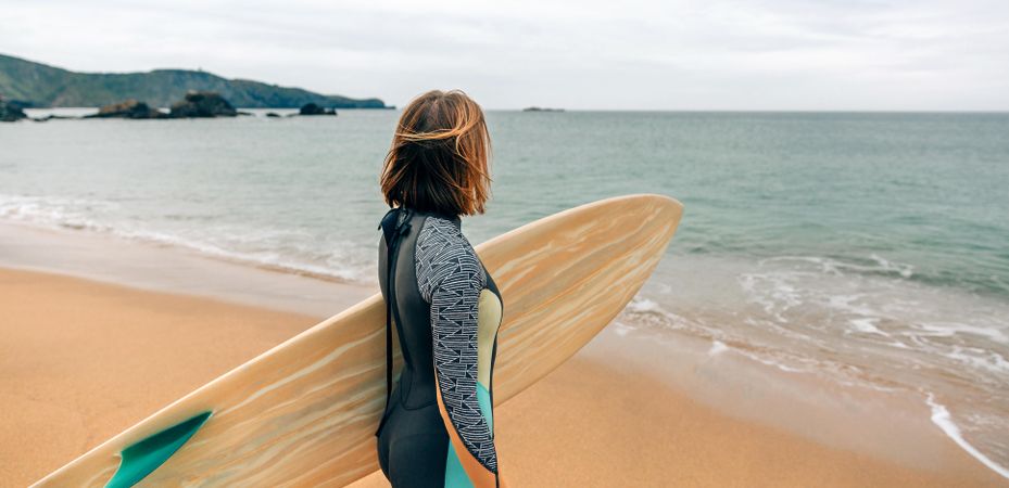 Woman standing on the coast with surfboard gazing out at beautiful ocean view
