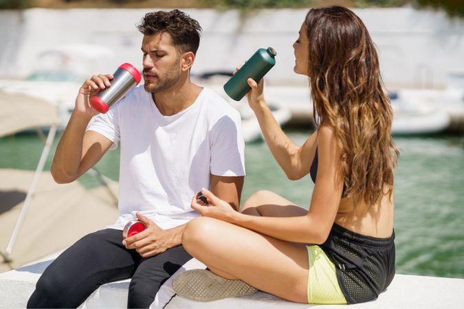 Couple drinking from water bottles on pier on sunny day