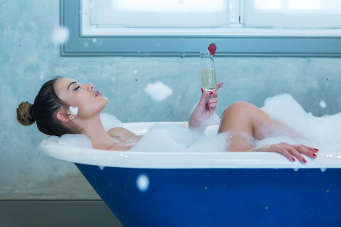 Woman in blue bathtub holding champagne glass