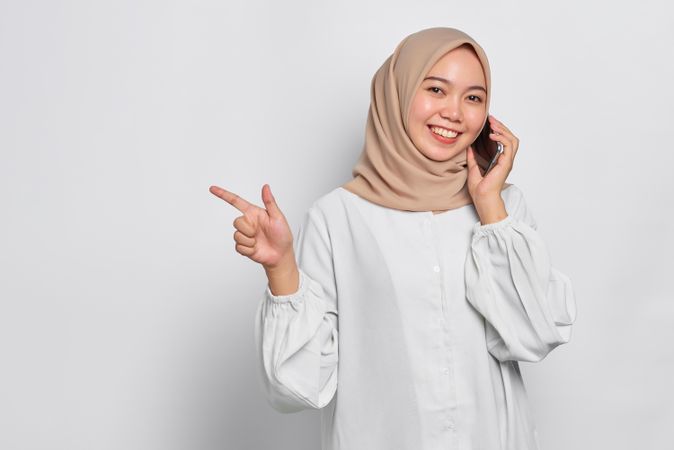 Asian Muslim woman using cell phone and pointing to copy space
