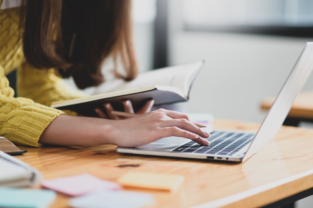 Female using laptop and holding a book in hand
