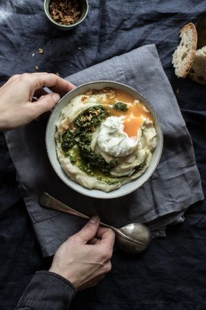 Person holding bowl with cauliflower puree with pesto and eggs
