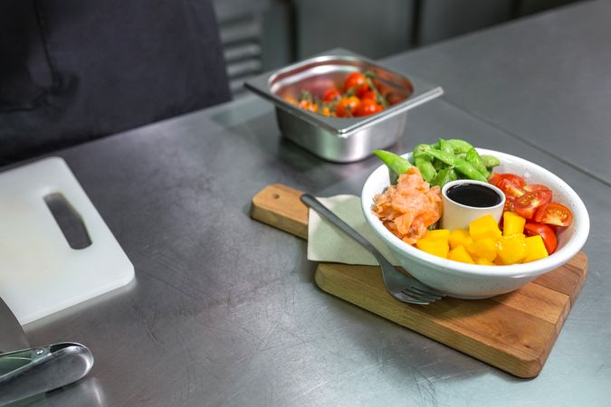 Salmon poke bowl served over wooden board on restaurant kitchen. Healthy and tasty food concept.