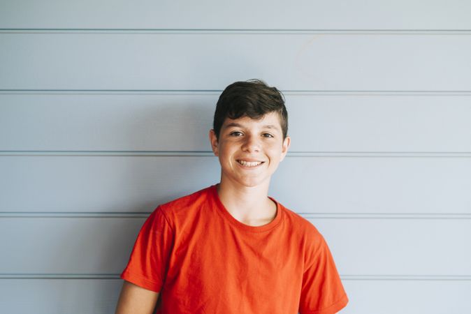 Portrait of a smiling male teen leaning on wall outside while looking camera