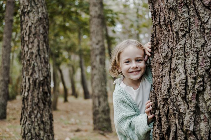Smiling girl behind tree in forest