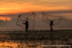 Silhouette of two fishermen with conical hat throwing their fishing net into water at sunset 5qLp10