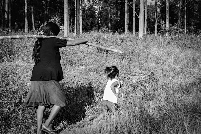 Grayscale photo of a mother holding a wooden stick and walking with her daughter in the woods