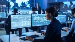 Financial Analyst Examines Real-time Market Data on Dual Monitors in High-tech Trading Room.
