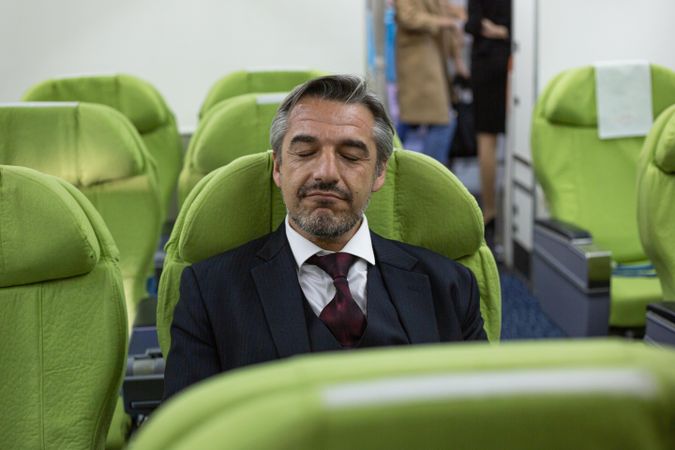 Male sitting in business attire with eyes closed on flight