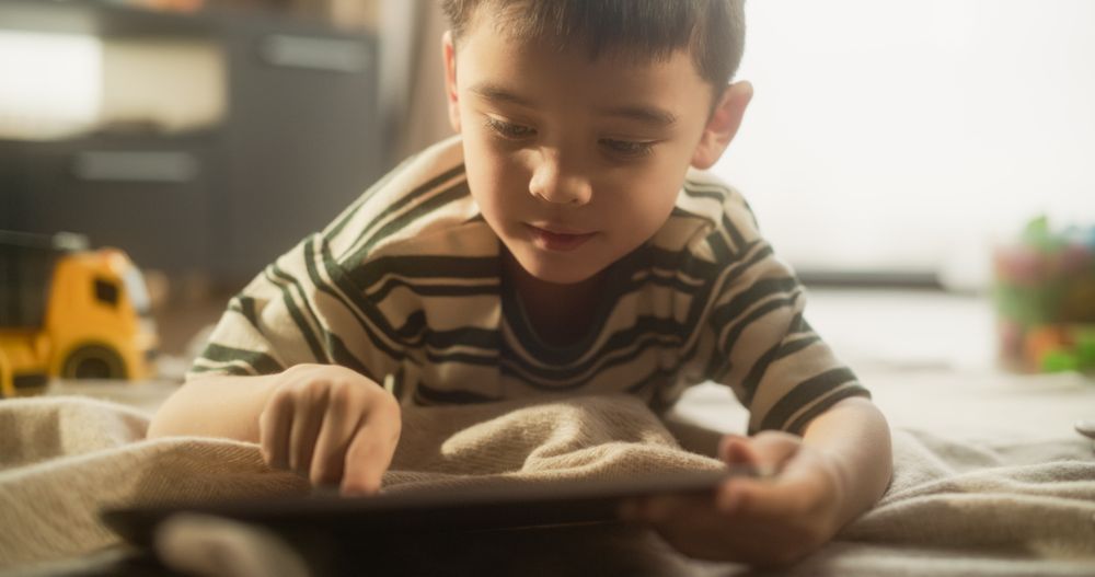 Portrait of a Focused Asian Male Kid Using Digital Tablet in his Room.