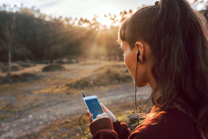 Young woman with piercing listening music on smartphone on hill