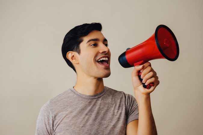 Hispanic male holding red loudspeaker to his face, side view