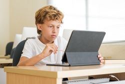 Clever schoolboy using tablet in classroom