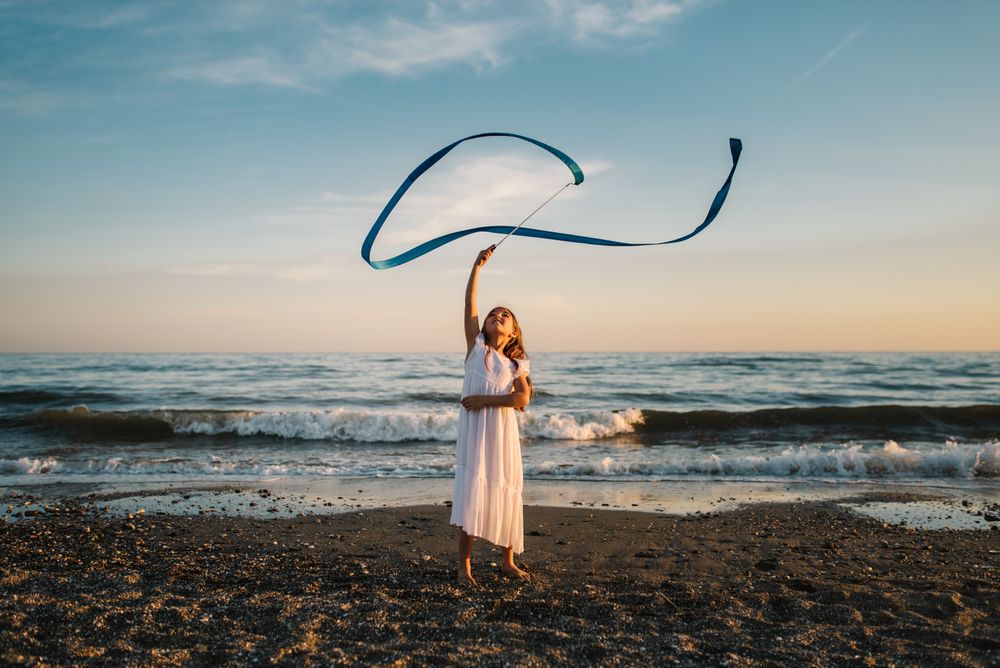 Adorable girl playing with ribbon on seaside