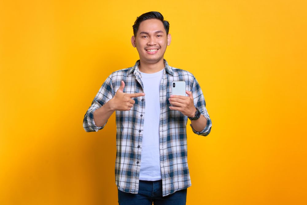 Smiling Asian male holding his phone and pointing at it