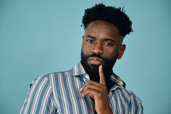 Closeup portrait of a serious Black man in blue studio shoot with finger to chin