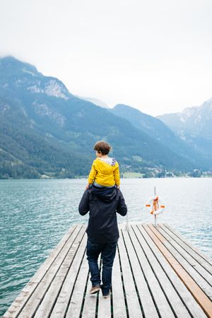 Man with kid on neck walking along pier