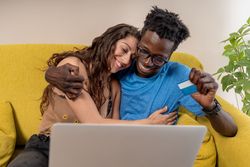 An affectionate diverse couple hugging happily after making a successful online purchase with a credit card.