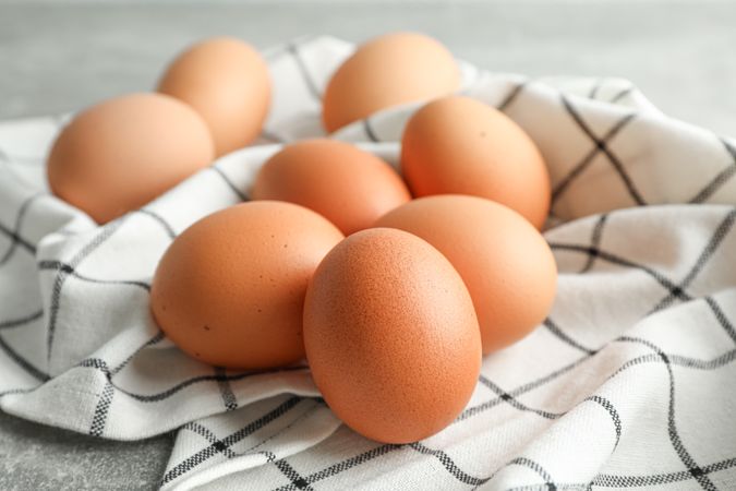 Brown chicken eggs in kitchen towel on grey background, space for text
