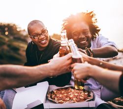 Two people smiling as the group toasts with beer over pizza at sunset