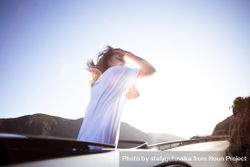 Woman standing out through a vehicle’s sunroof running her hands through her hair 4dXkN4
