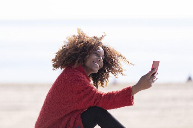 Side view of female taking picture on smart phone on bench on the coast