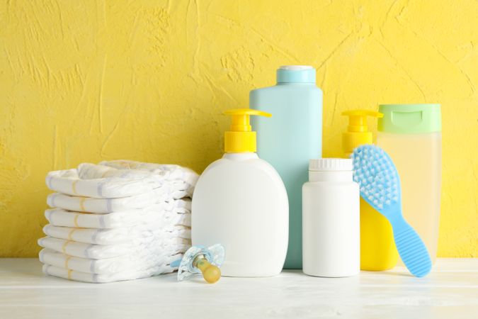 Baby hygiene accessories on wooden table against yellow background