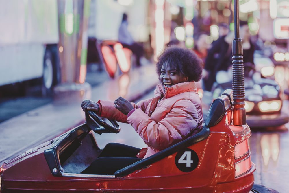 Excited Black woman riding car in amusement park