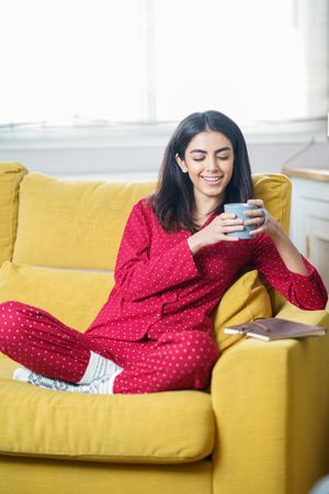 Vertical composition of female sipping tea on yellow sofa at home