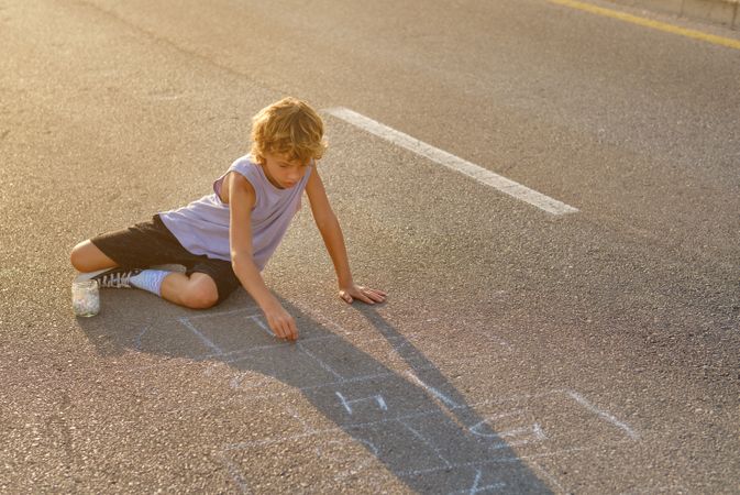 Boy drawing hopscotch on asphalt road