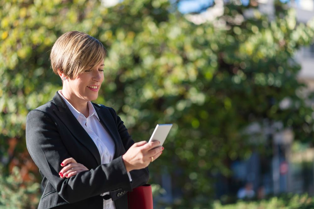 Happy businesswoman checking phone screen in front of hedge