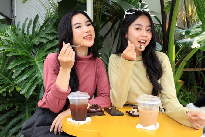 Two Young Asian Girl Eating Dessert while Looking at Camera in an Outdoor Coffee Shop