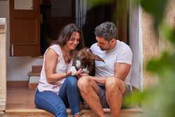 Happy couple caressing dog on porch of house