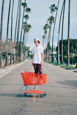 Young man standing near a red shopping cart in the middle of the road