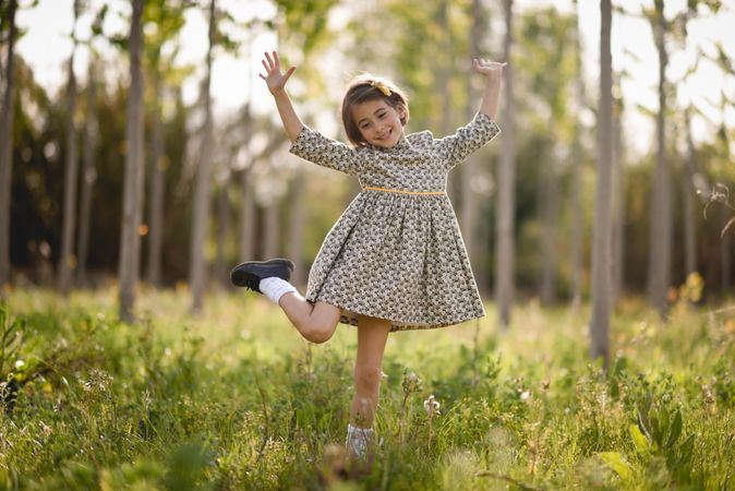 Happy child standing in dress in field surrounded by trees