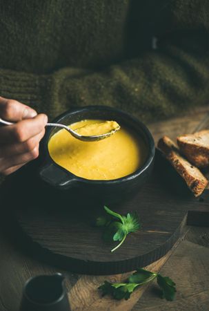 Man eating warm yellow soup from dark bowl with toast