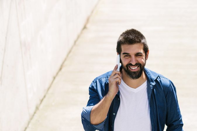 Smiling man in denim walking outside talking on phone