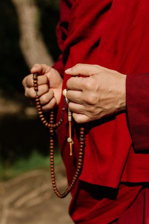 Cropped image of Buddhist monk holding prayer beads standing outdoor