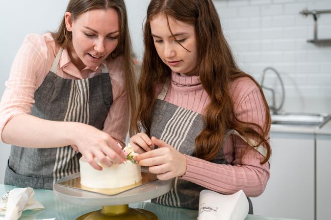 Mother helping little girl to decorate homemade cake