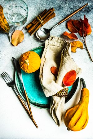 Top view of fall table setting with colorful leaves, gourd and cinnamon sticks garnishing teal plate